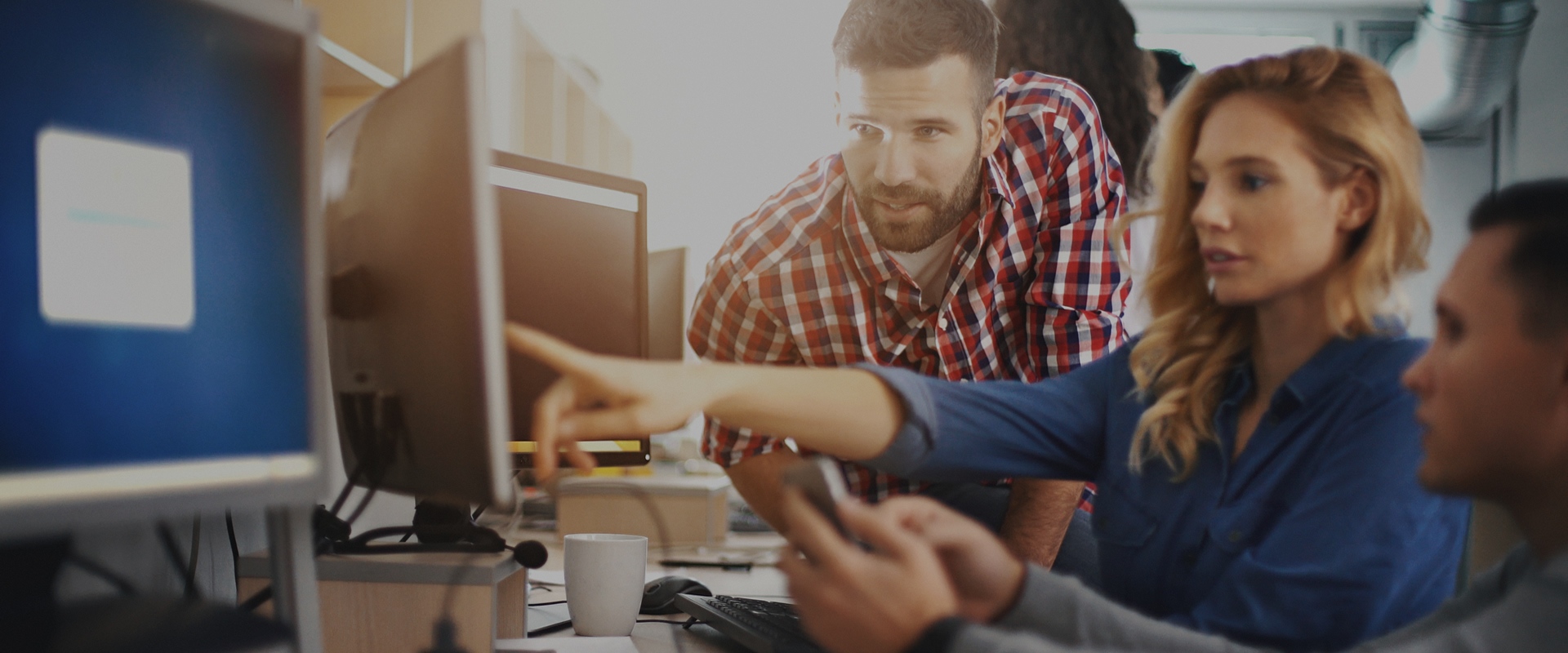 A woman pointing something on the monitor while two men watch